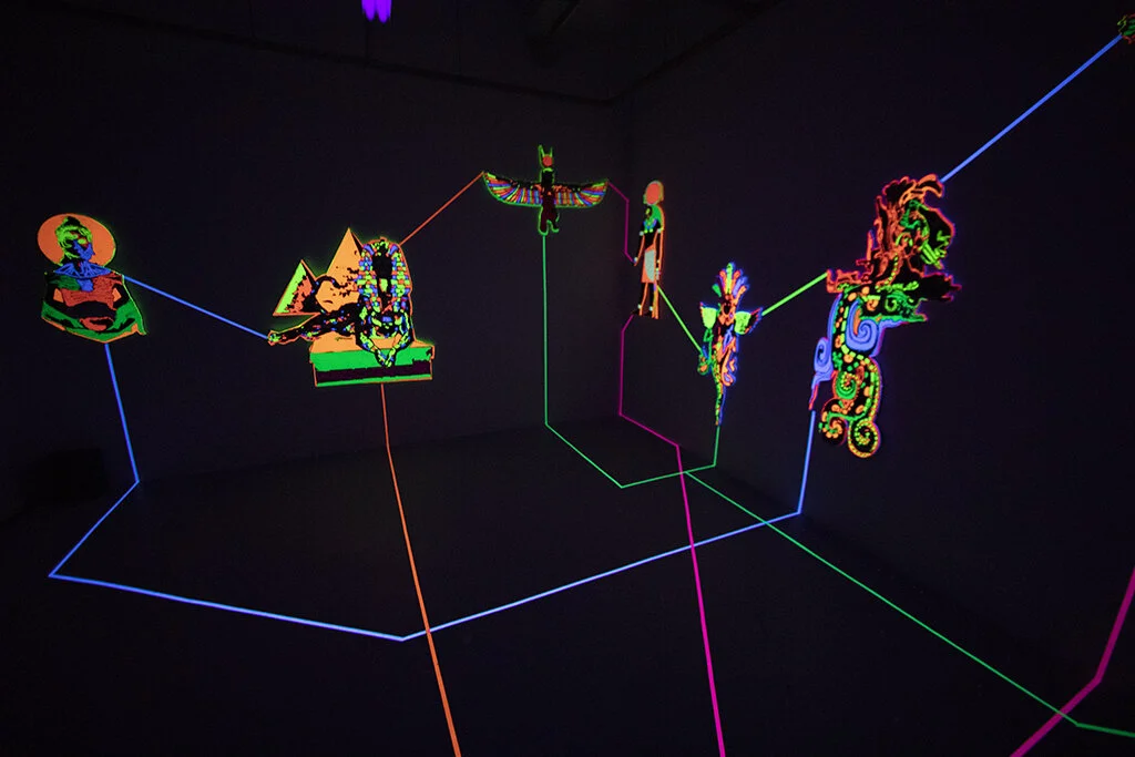 "Emanations" is an installation by artist Nafis Watson depicting deities that have been carved out using a CNC machine. The deities are painted in ultraviolet paint and connected to one another using ultraviolet tape. 