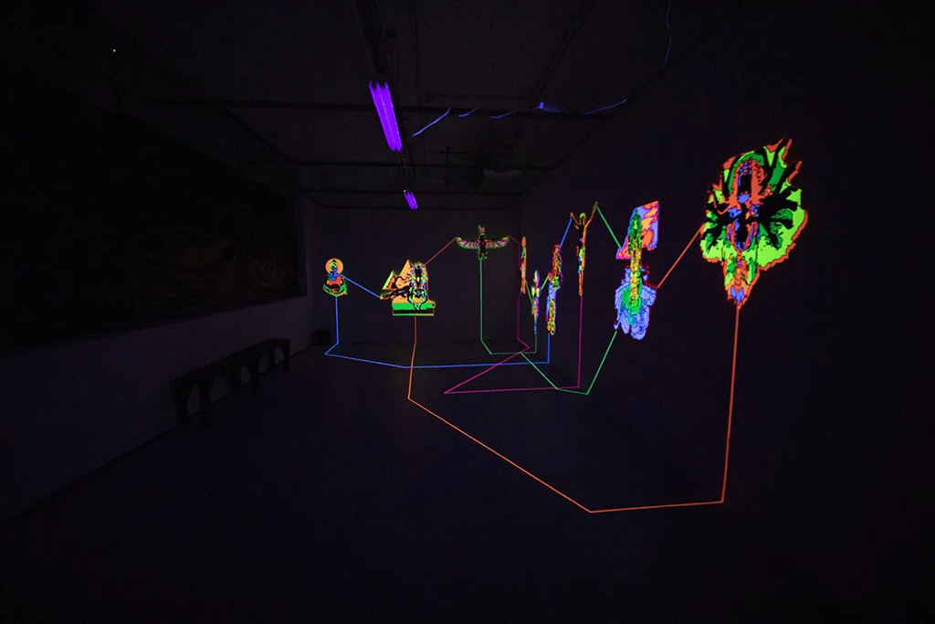"Emanations" is an installation by artist Nafis Watson depicting deities that have been carved out using a CNC machine. The deities are painted in ultraviolet paint and connected to one another using ultraviolet tape. 