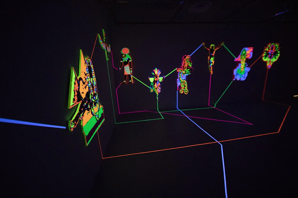 "Emanations" is an installation by artist Nafis Watson depicting deities that have been carved out using a CNC machine. The deities are painted in ultraviolet paint and connected to one another using ultraviolet tape. 