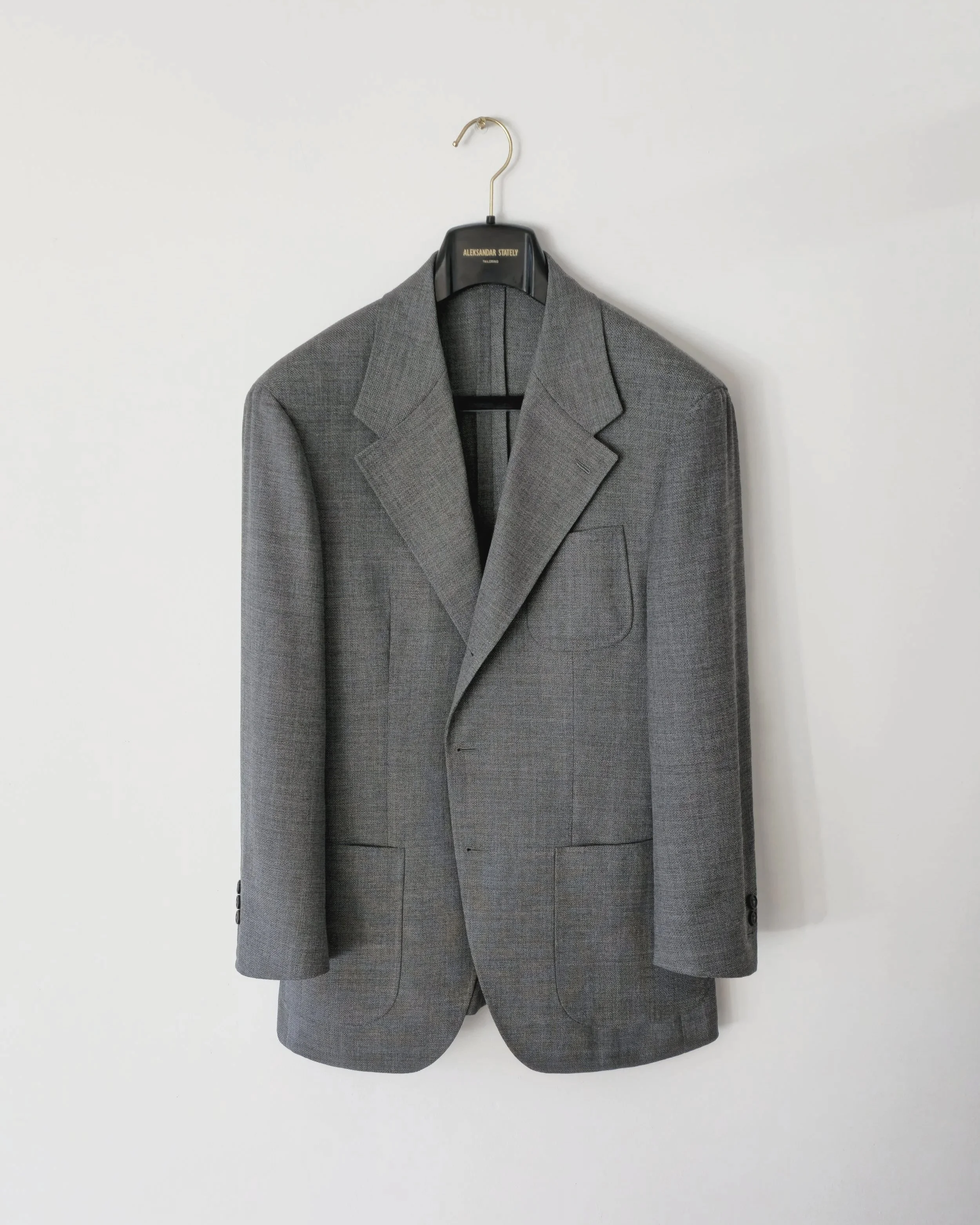 Aleksandar Stately Grey Hopsack Made to Measure tailored jacket on a black Aleksandar Stately hanger against a plain white wall Brisbane Australia.
