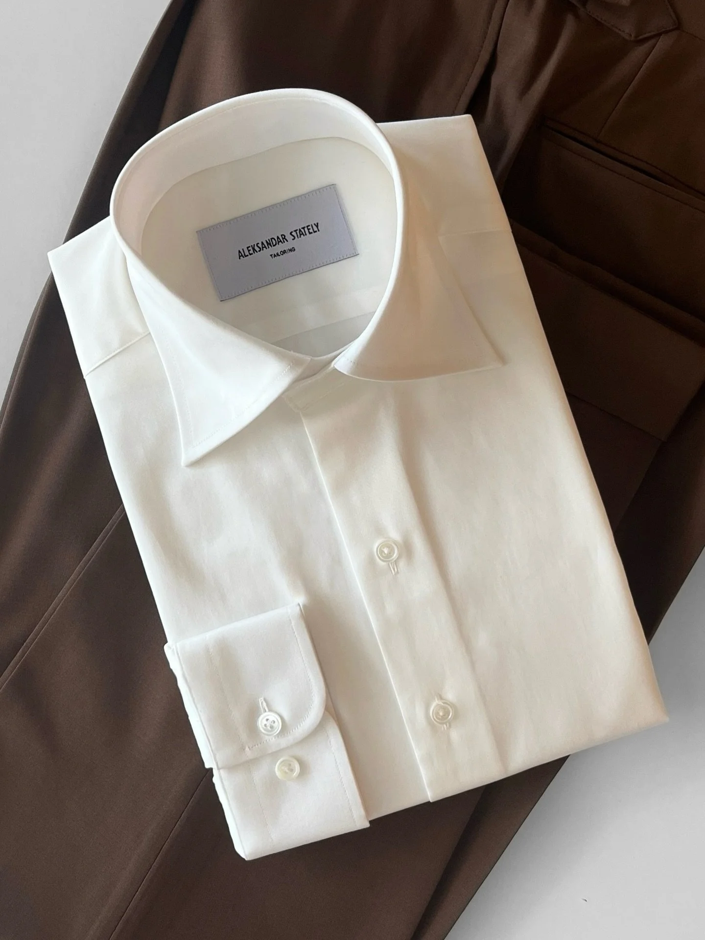 A timeless ensemble featuring a made-to-measure off-white shirt paired with tailored chocolate-brown trousers.