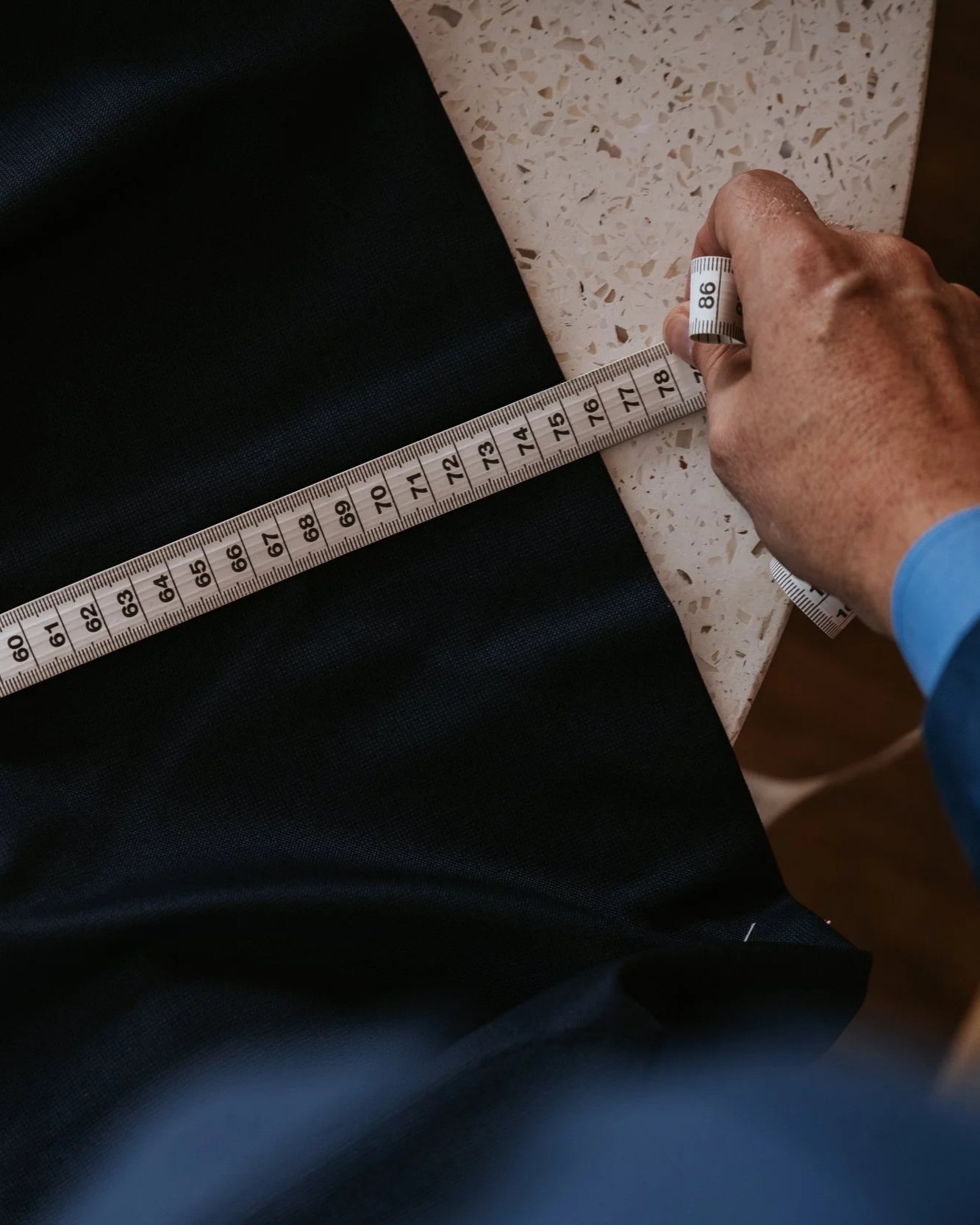 A person's hand holding a measuring tape with a black garment placed on a surface, the tape stretched across the fabric.