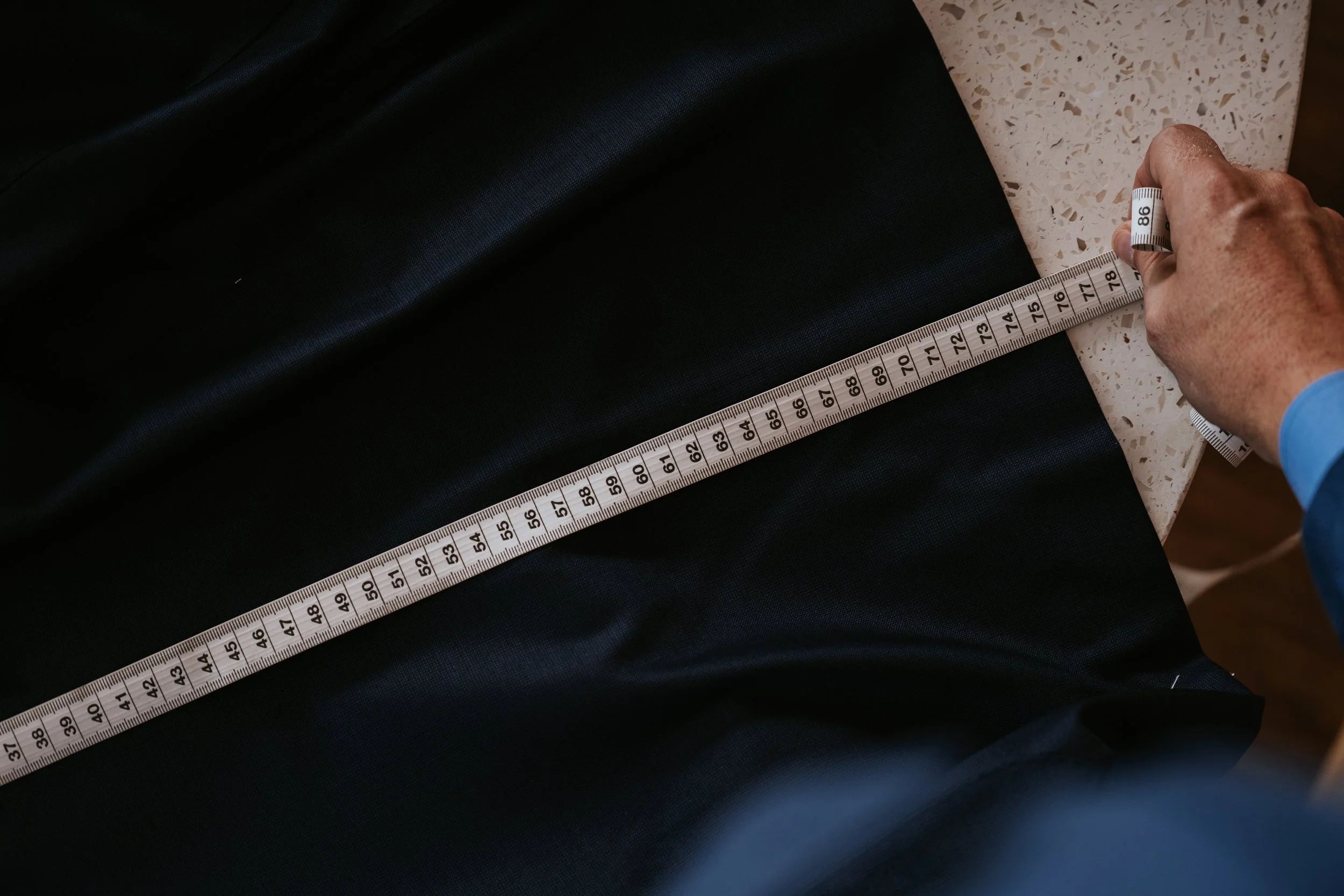 Aleksandar Stately measuring fabric with a measuring tape on a speckled countertop.