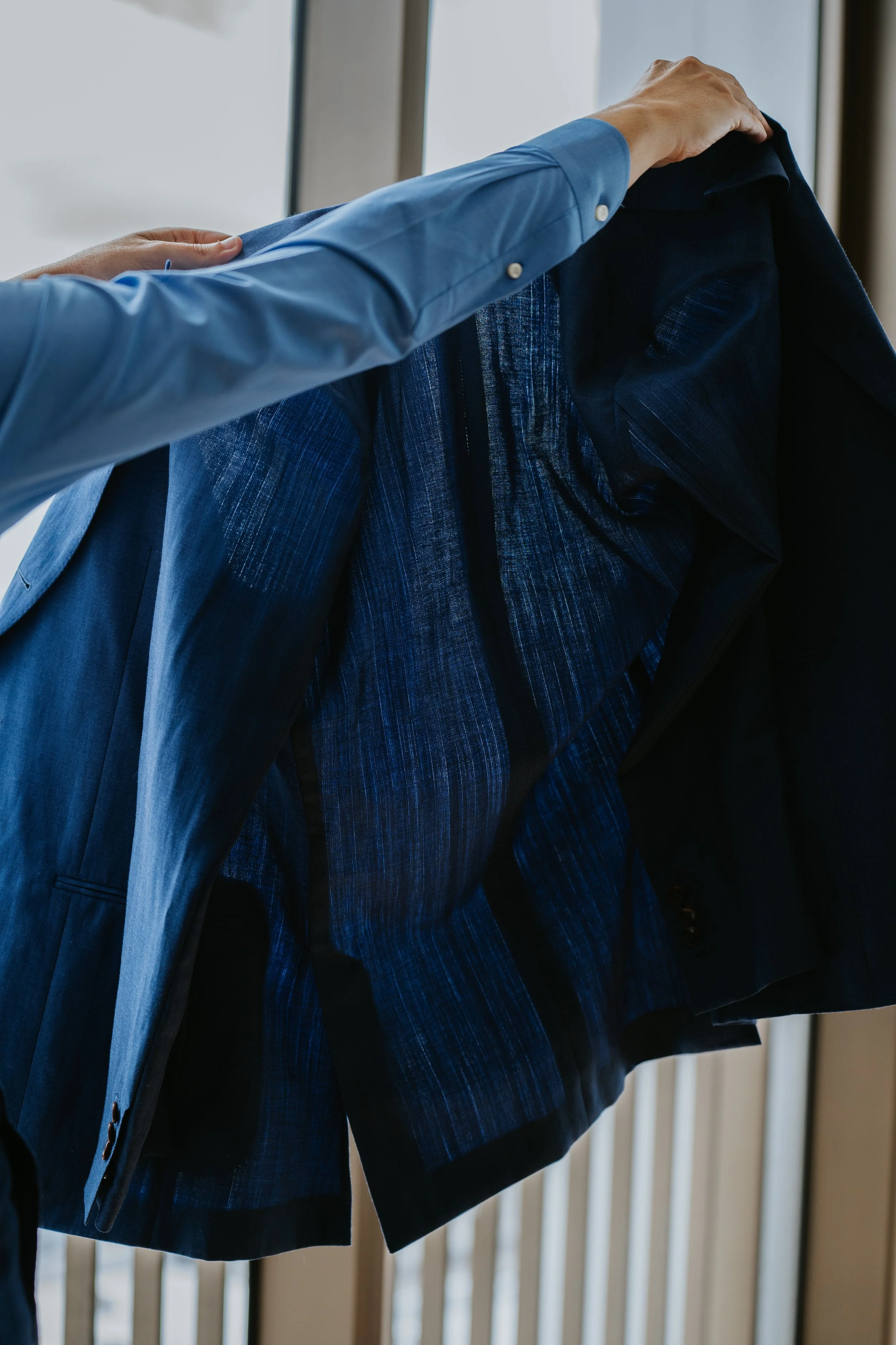ALEKSANDAR STATELY person in a light blue shirt placing a navy blazer on a hanger.