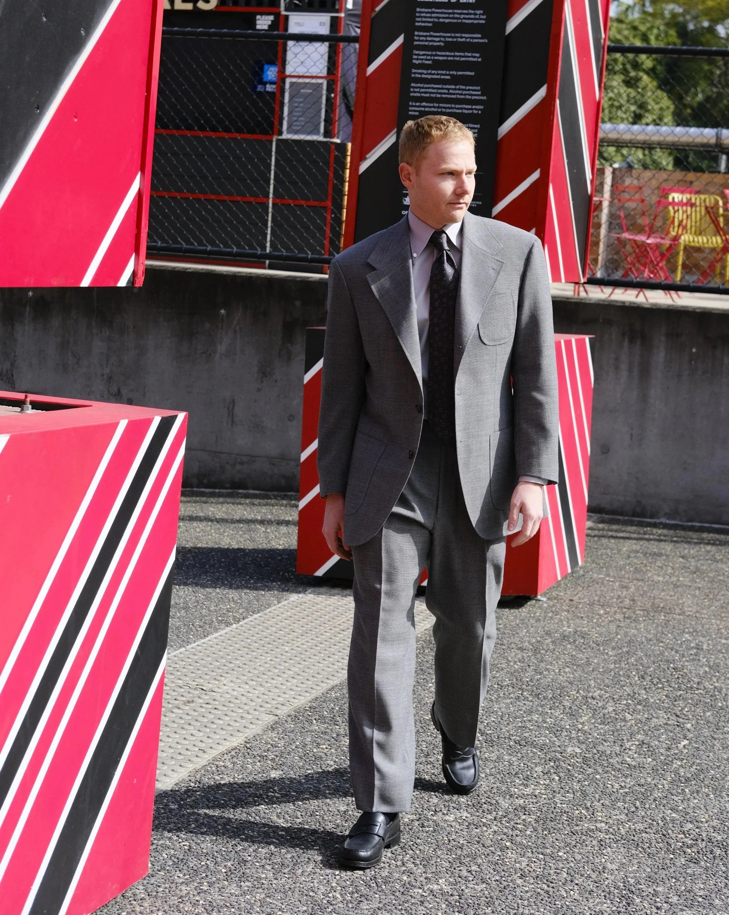 A man in a grey Aleksandar Stately custom tailored made to measure suit, black dress shoes, and a hand made Aleksandar Stately tie walks outdoors in Brisbane.