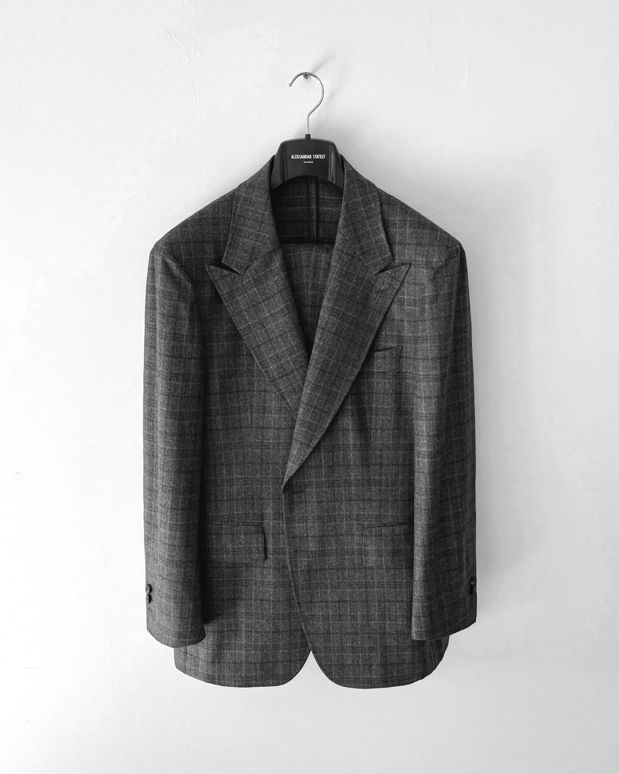 A ALEKSANDAR STATELY gray plaid suit hanging on a black hanger against a plain white wall.