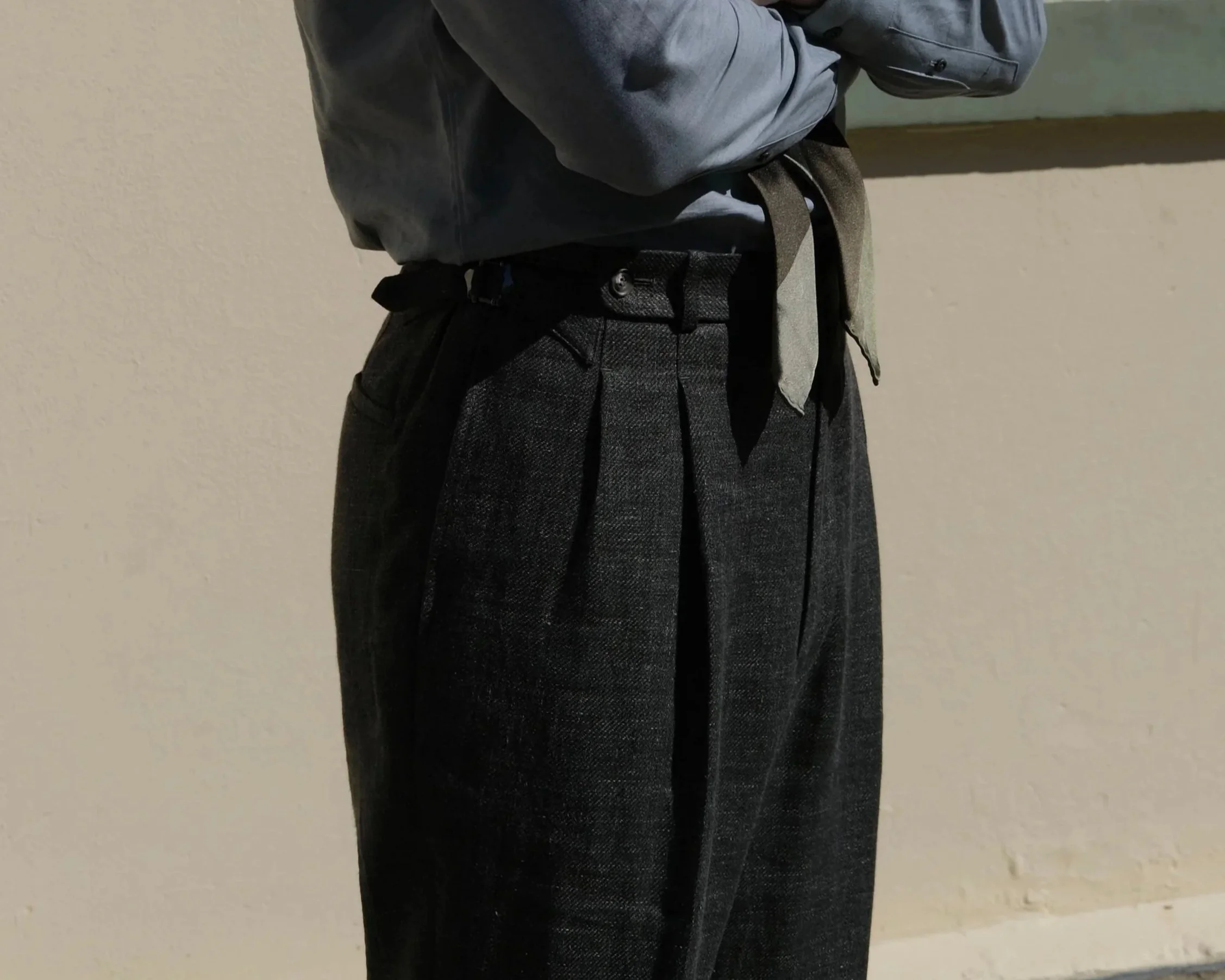 Close-up of a person wearing custom tailor made to measure Aleksandar Stately gray shirt and dark green pants against a beige wall