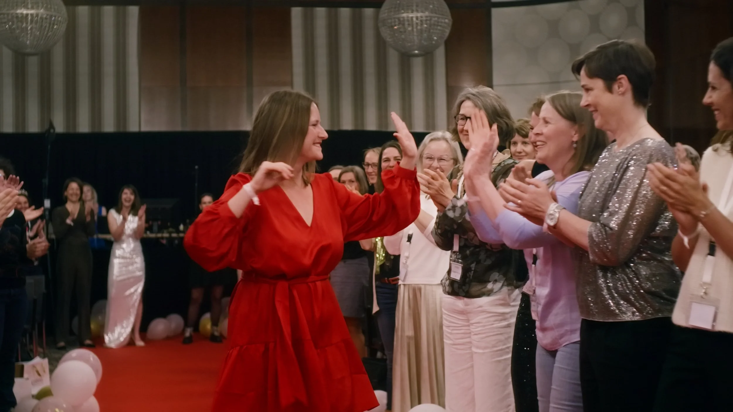 Frauen feiern auf einer festlichen Veranstaltung, lachen und klatschen, trägt elegante Kleidung, in einem edlen Innenraum mit Kronleuchtern.