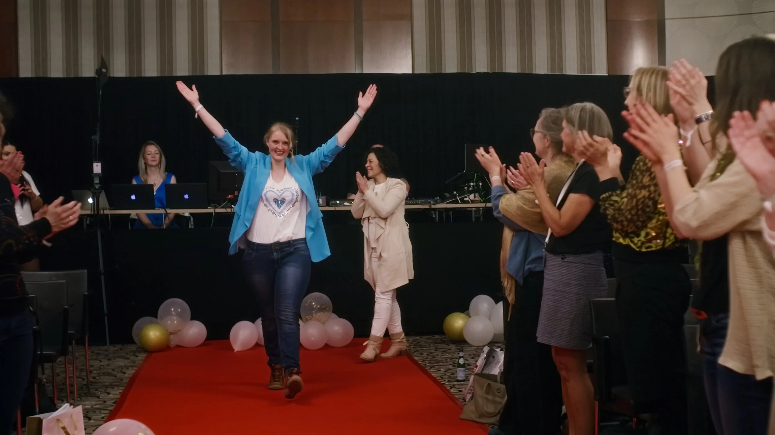 Freudige Frau läuft auf roten Teppich, umgeben von applaudierenden Menschen bei Feierlichkeit, Dekoration mit Ballons.