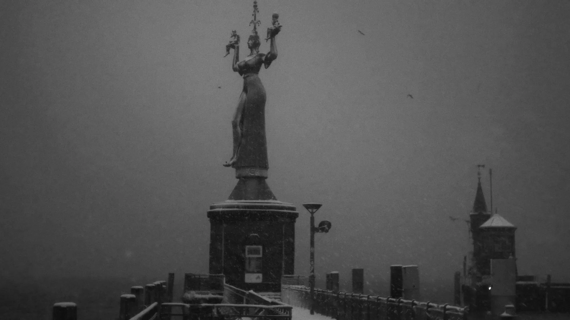 Schnee bedeckt den Hafenkran und die umliegenden Gebäude im düsteren Himmel.
