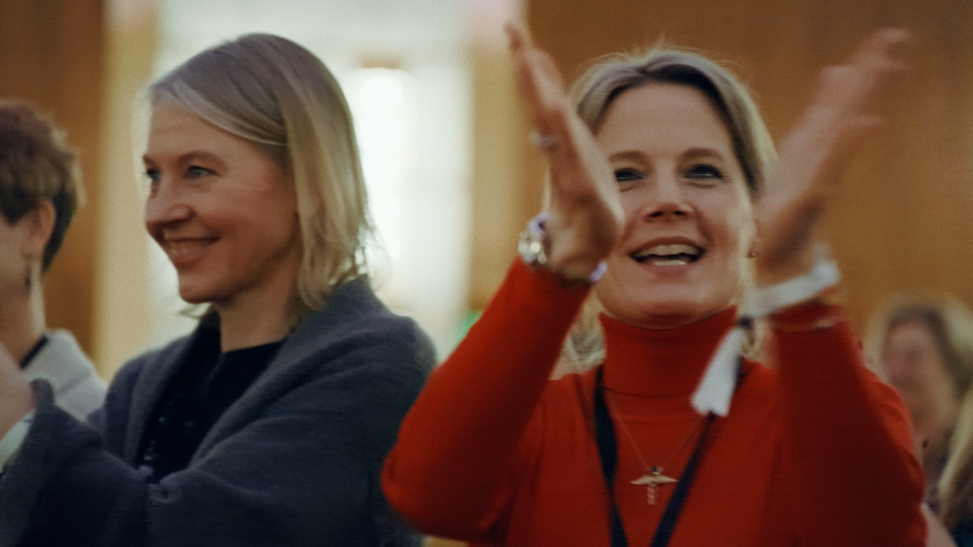 Zwei Frauen lachen und winken während einer Veranstaltung.