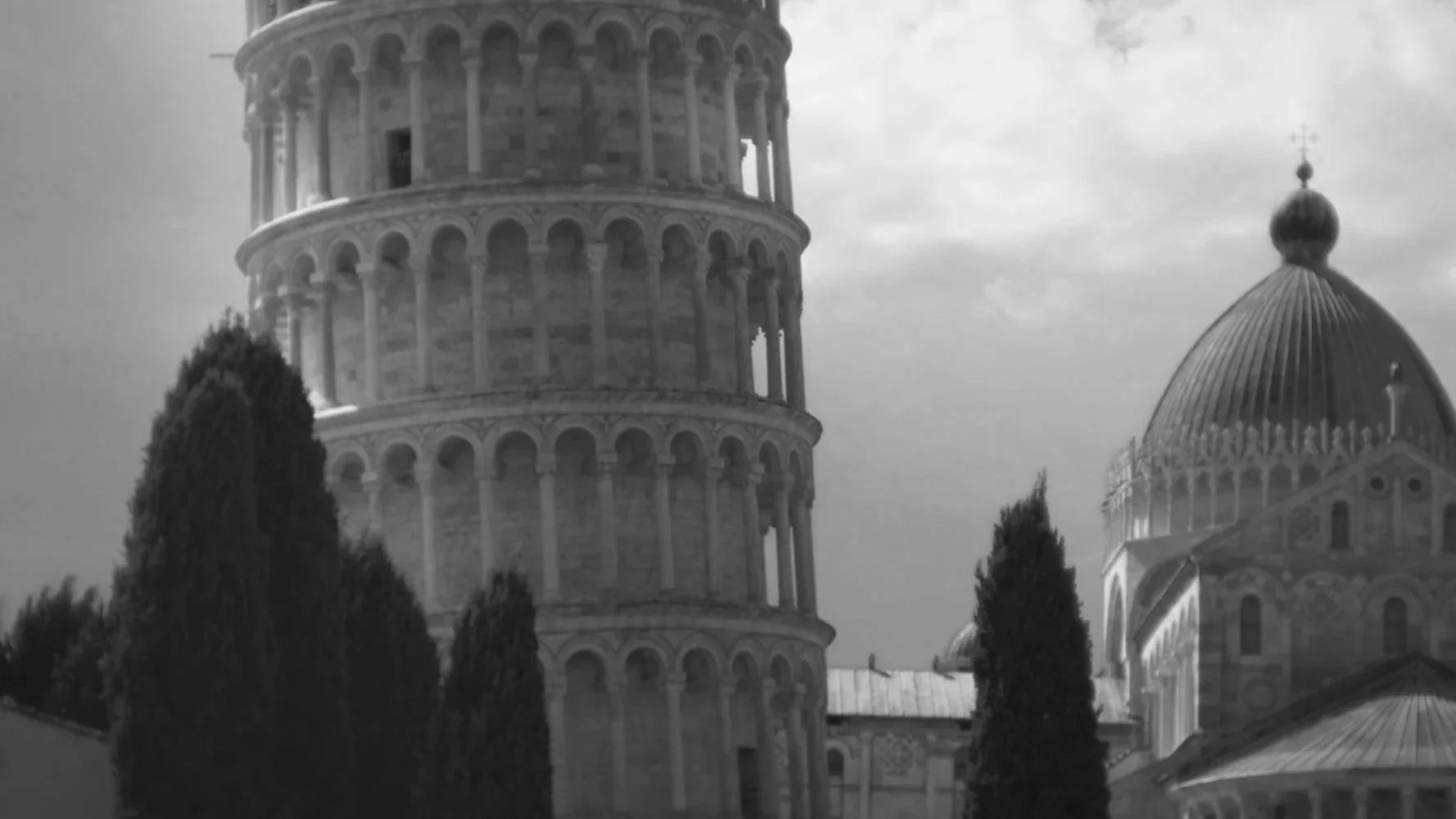 Schwarz-Weiß-Foto des Doms von Pisa mit seinem schiefen Glockenturm im Vordergrund, umgeben von Bäumen.