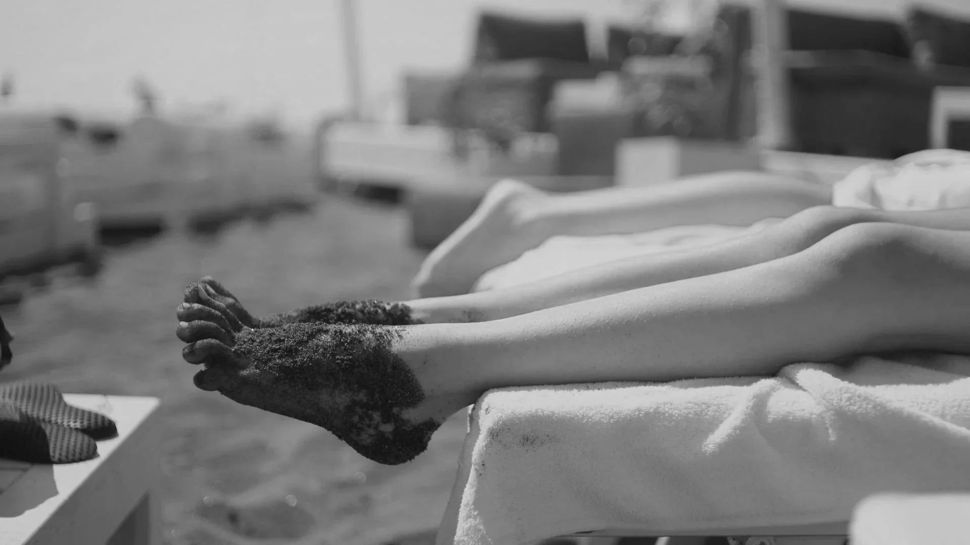 Zeichnung eines fallen gelassenen menschlichen Körpers auf einer Liege im Freien, Sand bedeckt die Beine, im Hintergrund Liegestühle und eine Strandlandschaft.