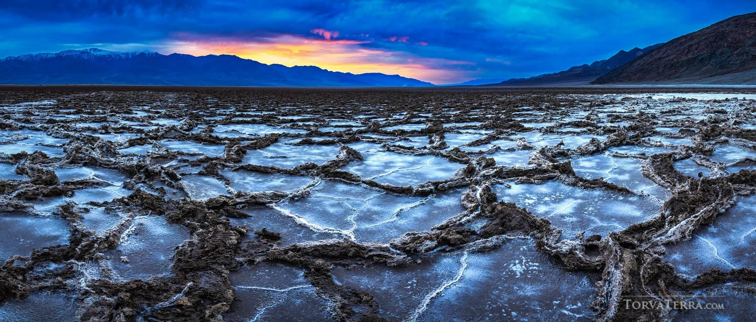 Salt flats with cracked surface and mountains in the background at sunset.