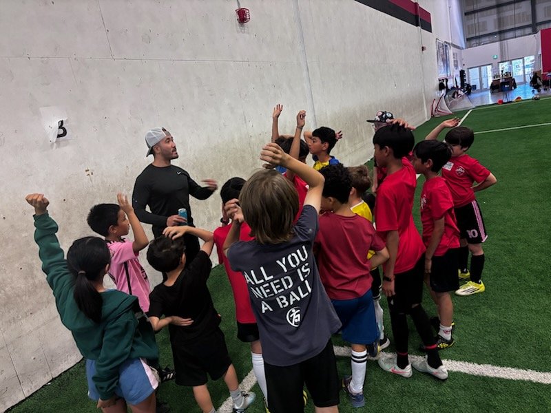 Group of children and coach in an indoor sports facility, possibly a soccer training session.
