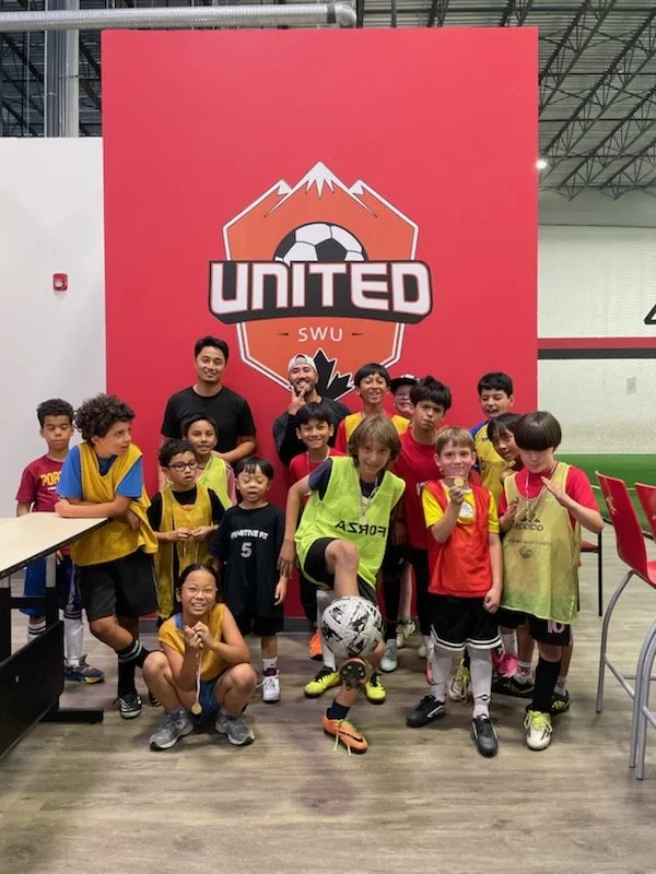 Group of children and coaches at a soccer event, posing in front of a red banner with a mountain and soccer ball logo labeled 'United SWU'.