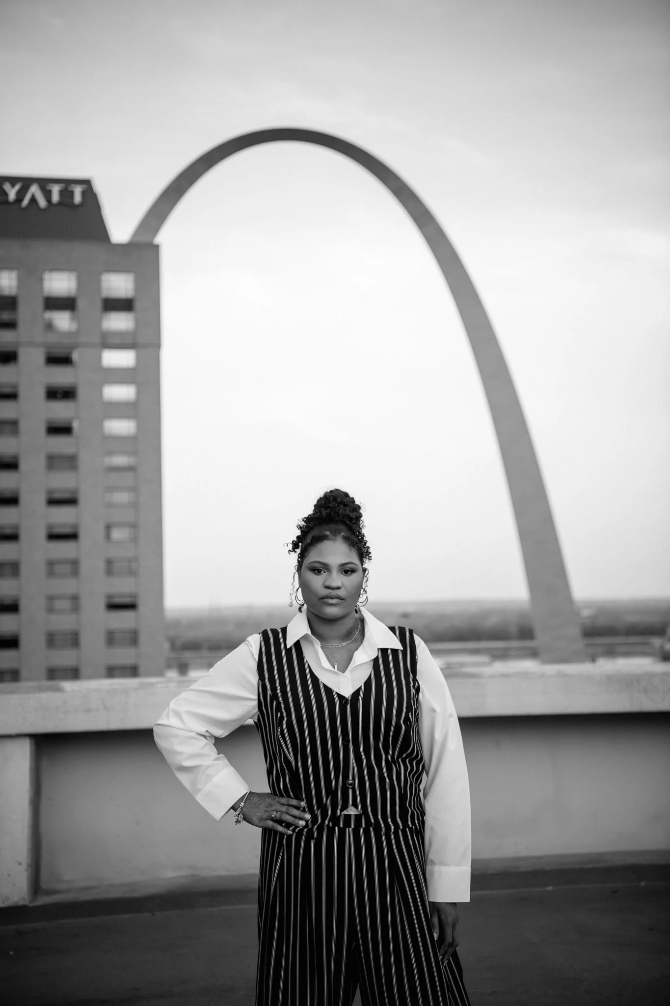 Stylish woman posing on a rooftop at sunset with a cityscape background, wearing a denim jacket and sneakers.