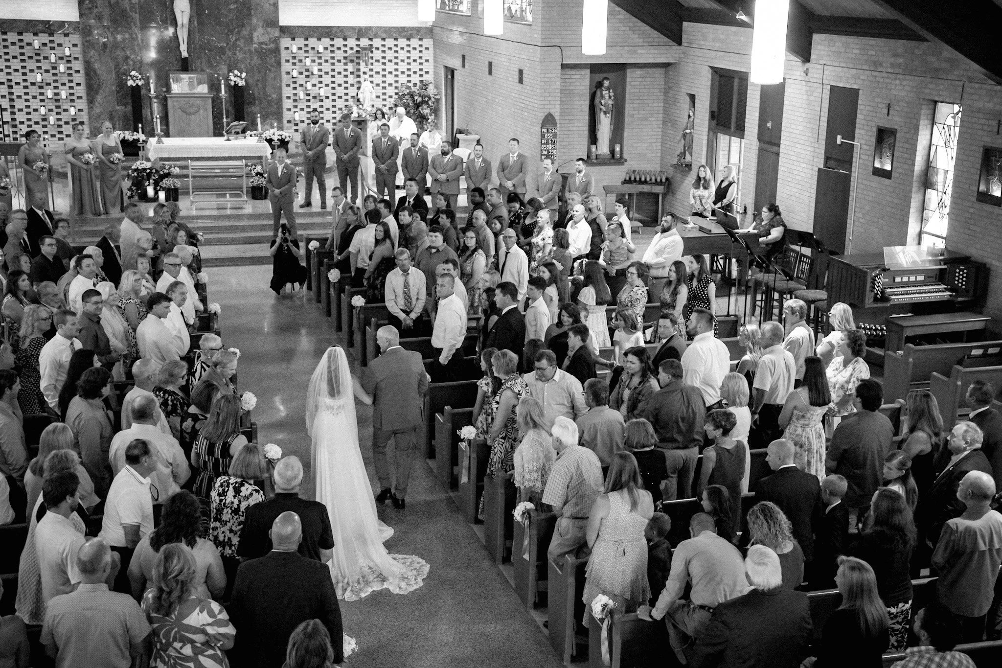 Bride being walked down the wedding ceremony aisle as guests watch