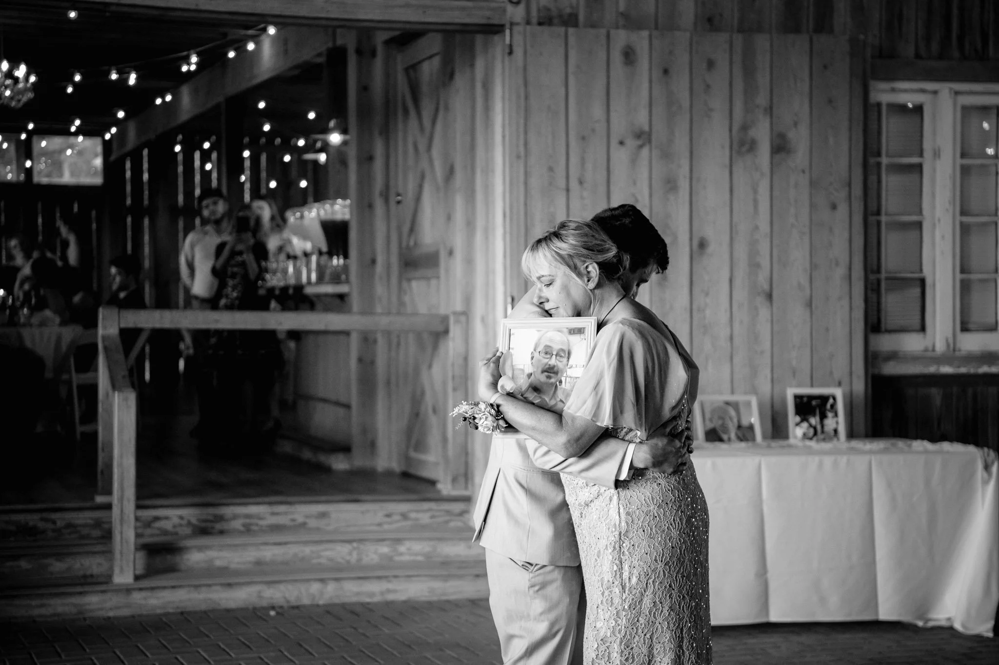 mother-of-the-groom dance while holding a photo of the groom's late father, an emotional portrait during wedding reception held at Chandler Hill Winery in Defiance, Missouri