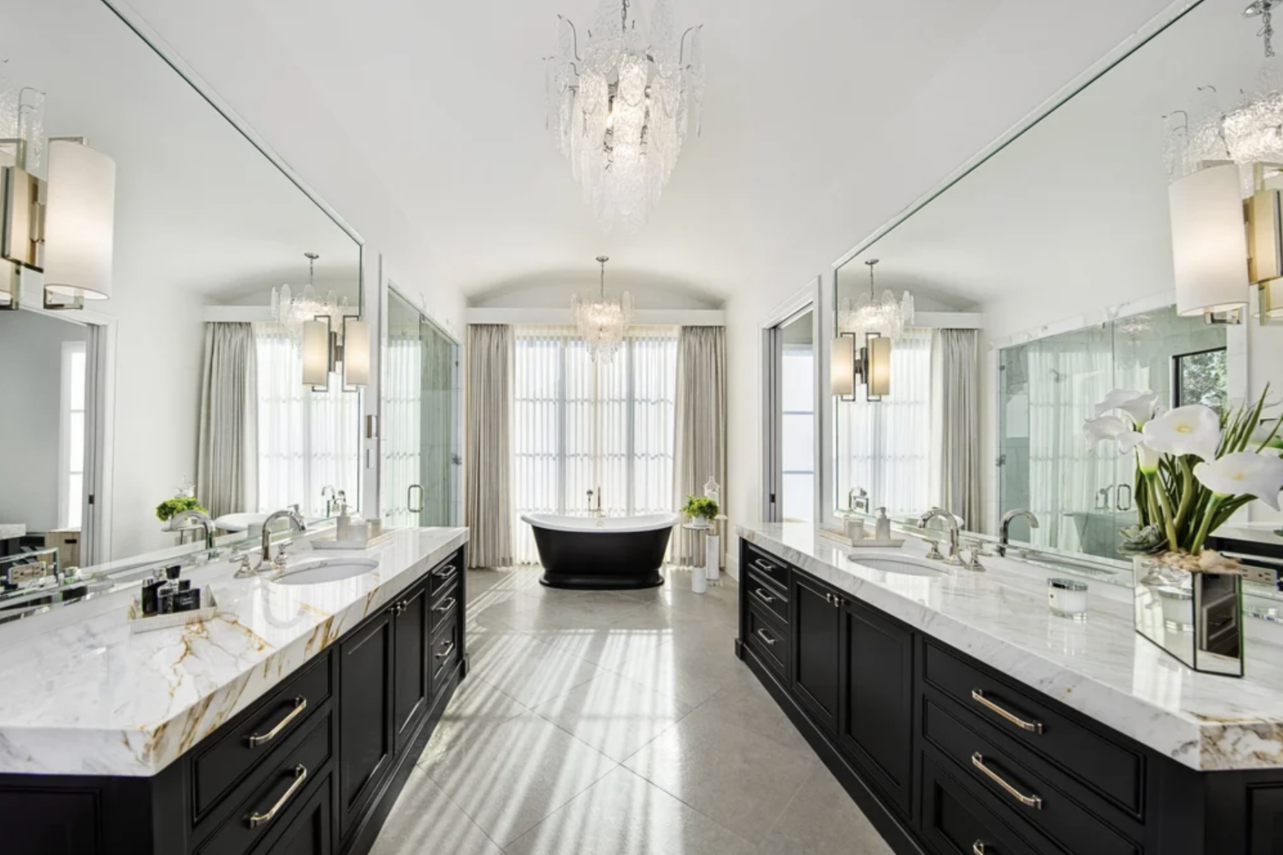 Luxury master bathroom with double vanity, marble countertops, black cabinetry, freestanding tub, and large mirrors with elegant lighting.