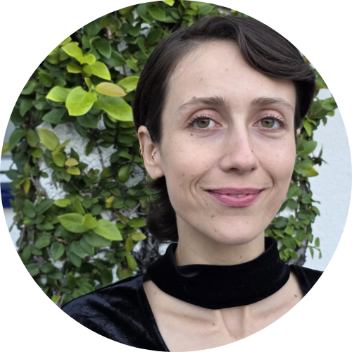 Image of Chels smiling with short brown hair, white skin & green eyes in front of a leafy background