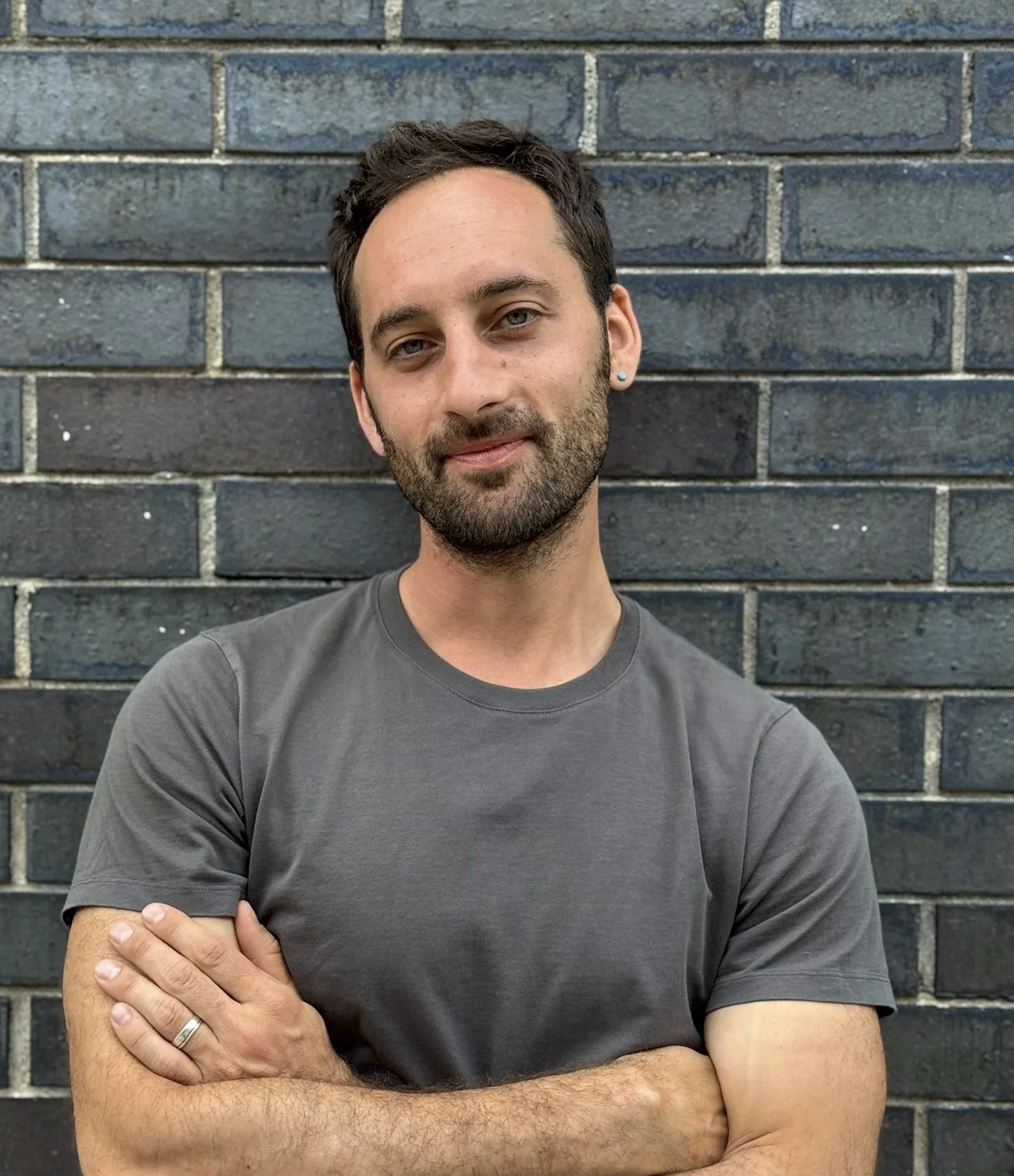 Portrait of Yotam Marom smiling, standing in front of a brick wall.