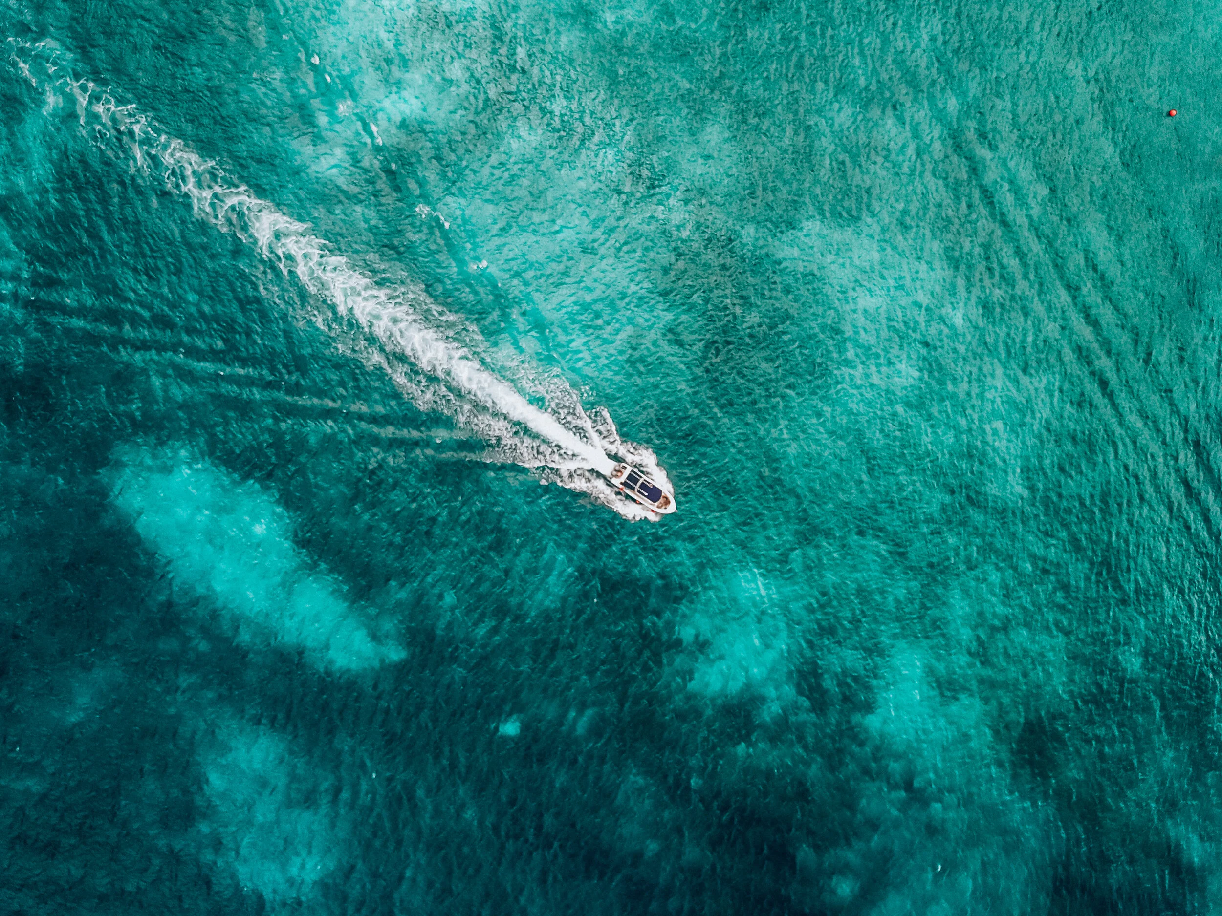 An aerial view of a boat moving through clear turquoise water, creating a white wake behind it.