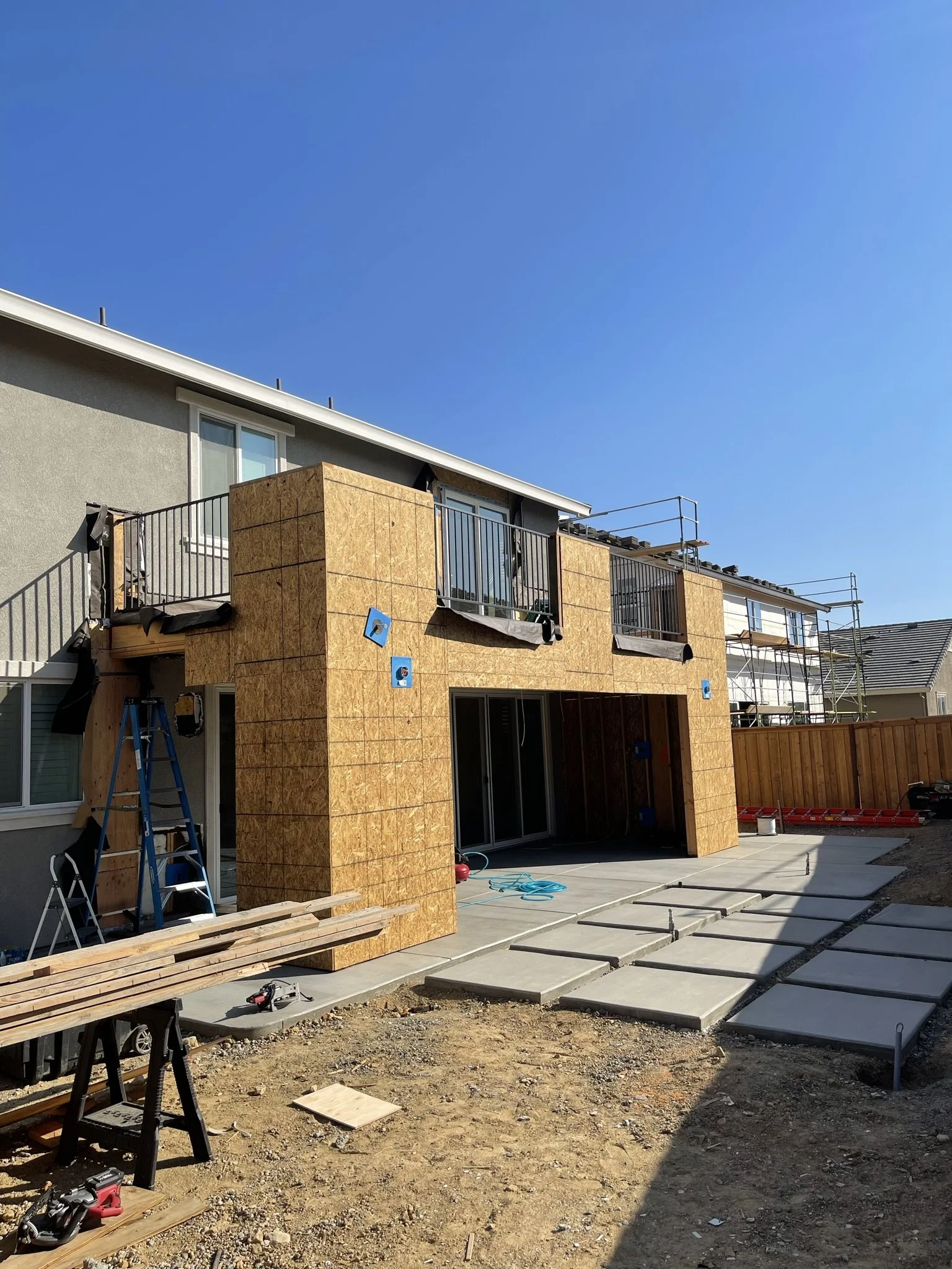 House under construction with OSB siding, scaffolding, and unfinished patio