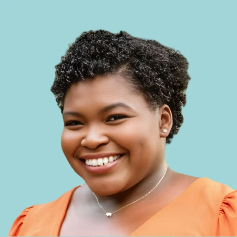 Close-up of a smiling woman with short curly hair wearing an orange top and a delicate necklace, against a gray background.