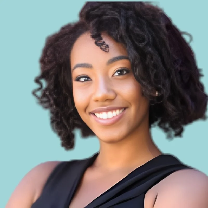 A young woman with curly dark hair smiling at the camera, wearing a black sleeveless top.