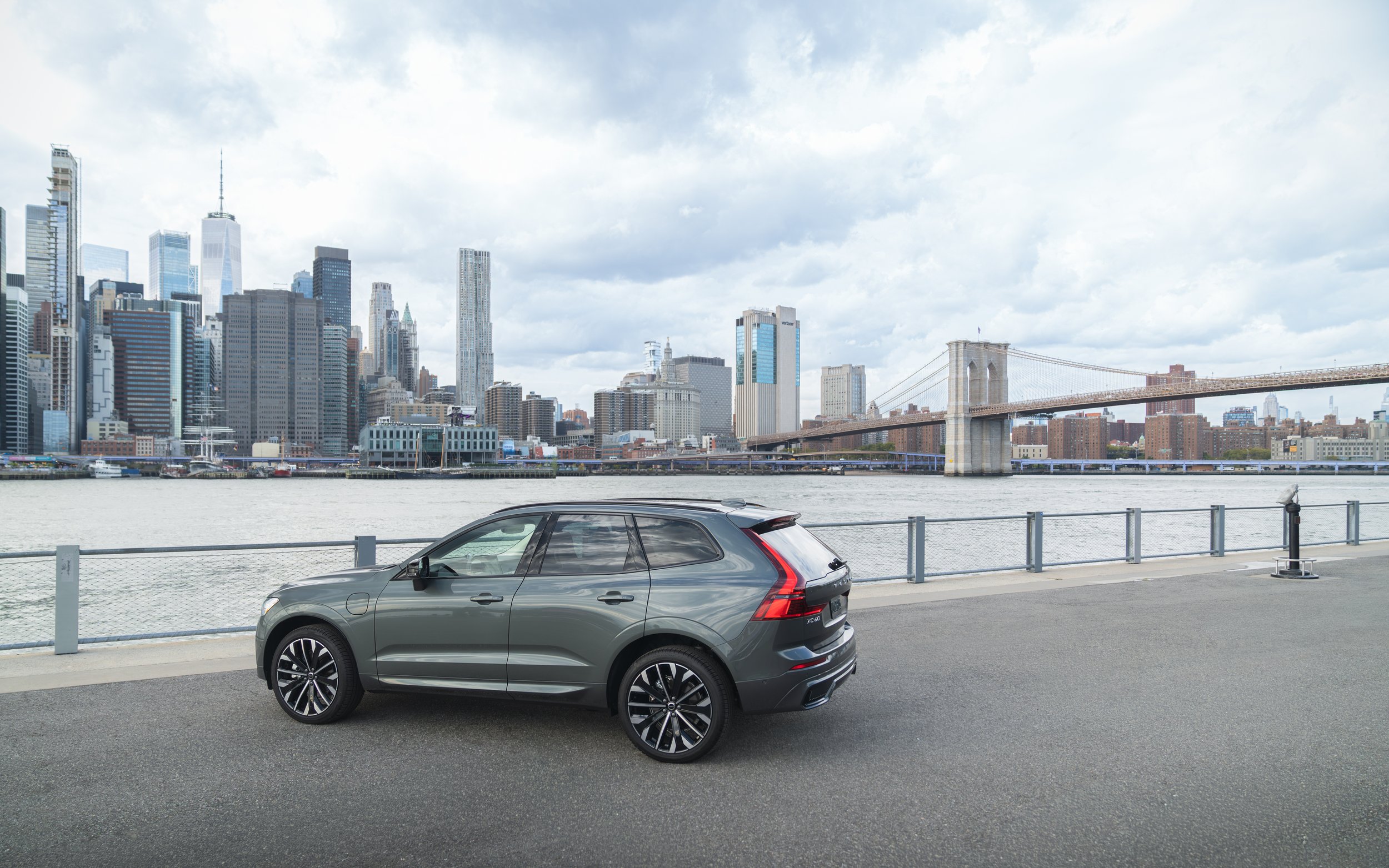 Volvo XC60 parked on a waterfront promenade with New York City skyline and Brooklyn Bridge in the background.