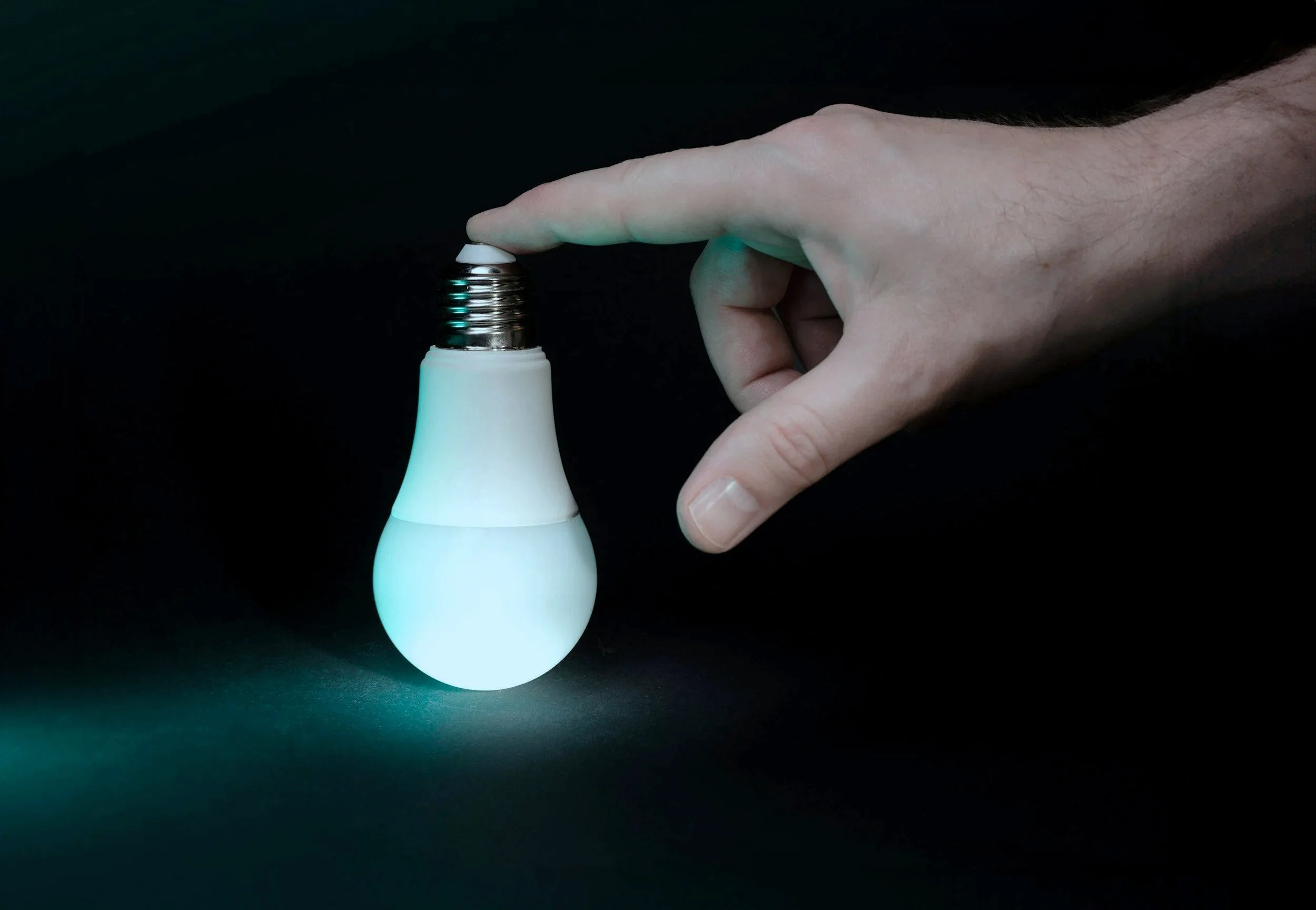 A hand adjusting a light bulb that is illuminated with a greenish glow against a dark background.