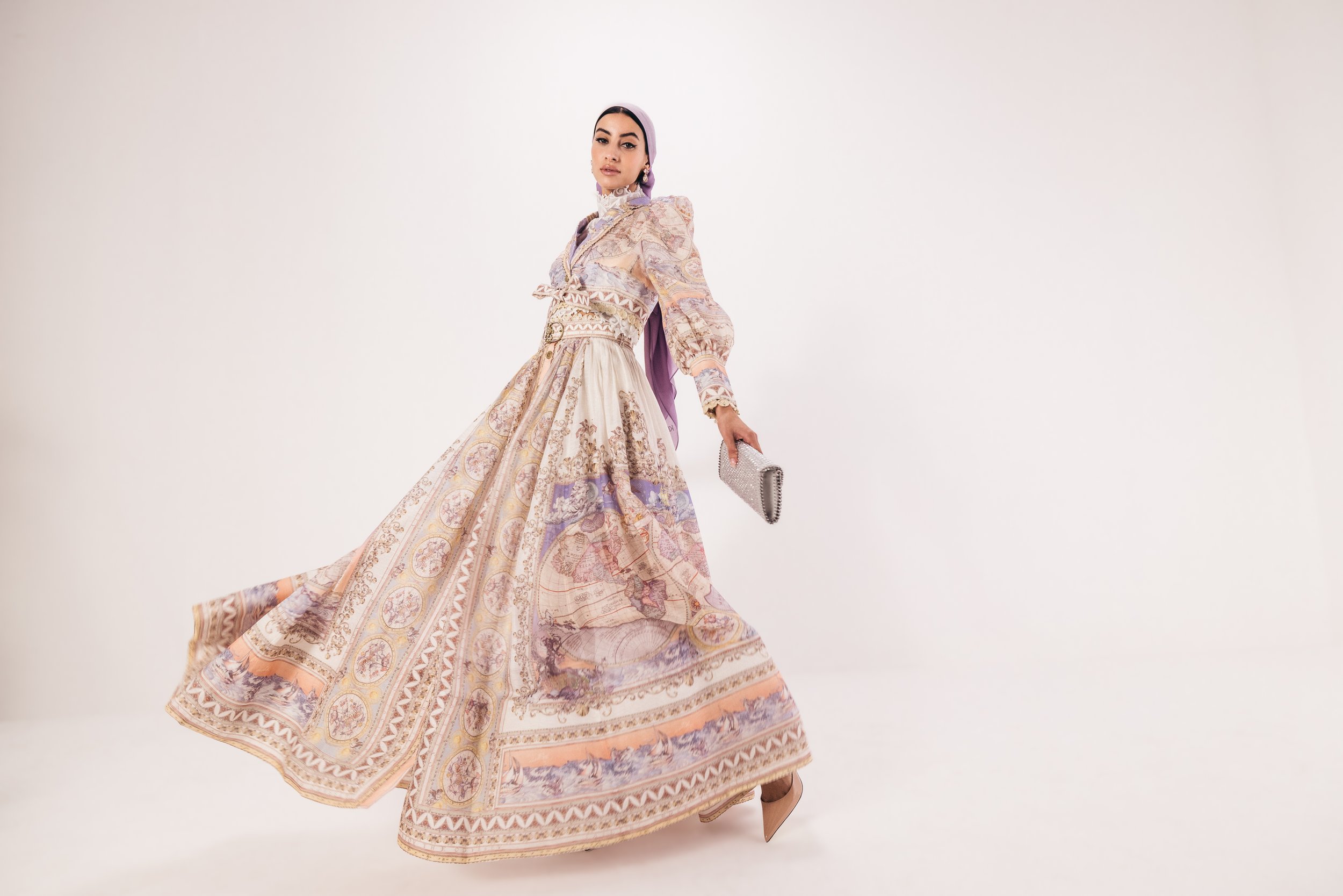 Woman in long, flowing, patterned dress with puffed sleeves, holding a clutch.