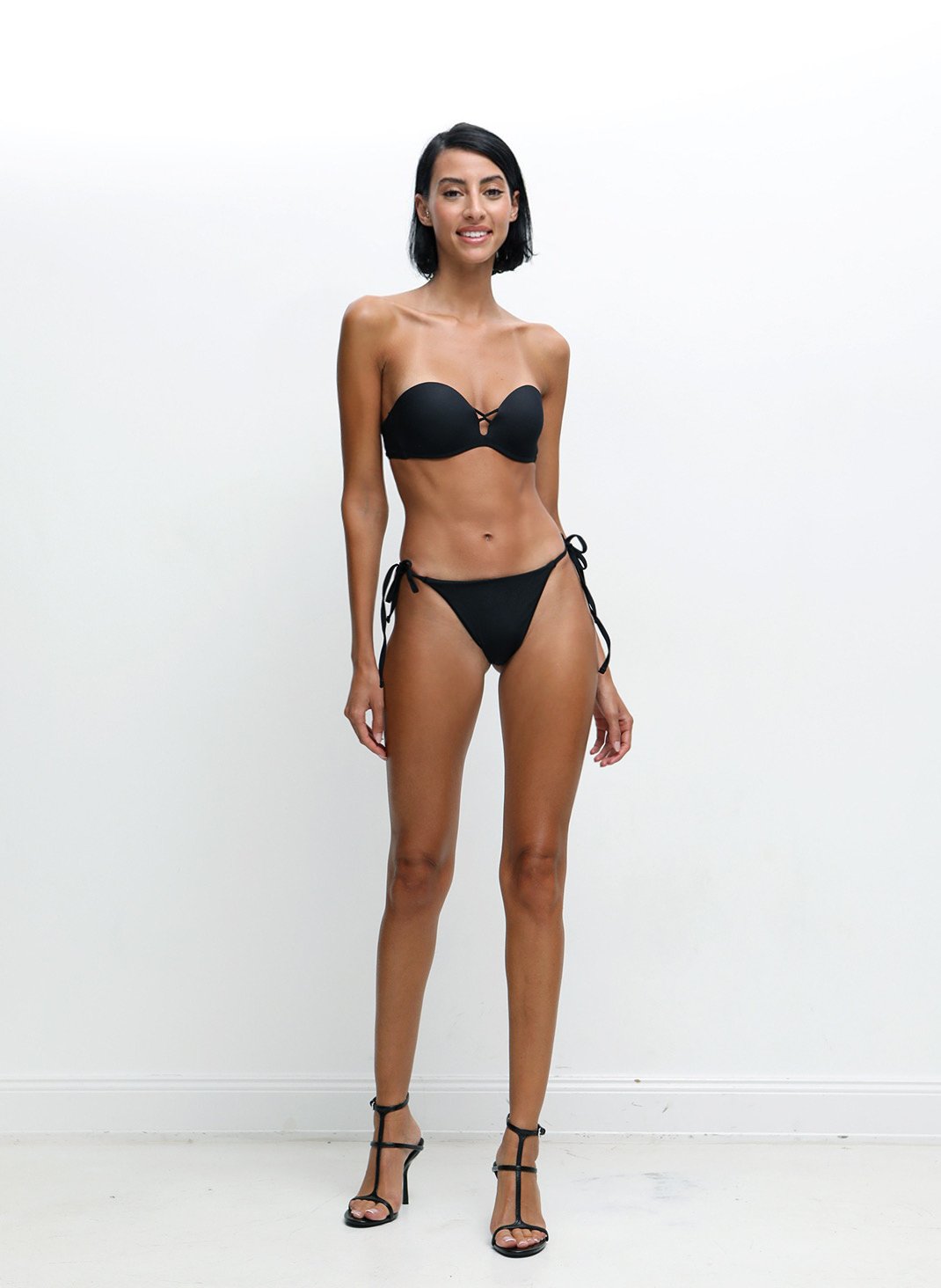 Woman in a black bikini and heels against a white background.