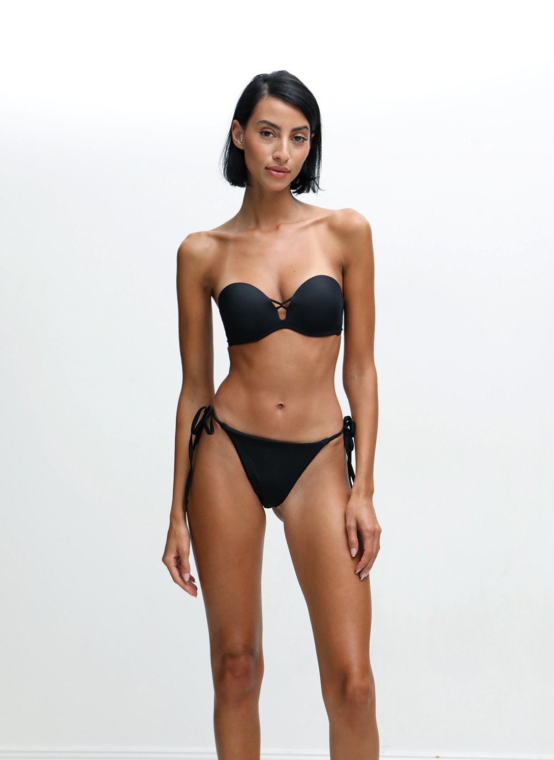 Woman in a black bikini posing against a white background.