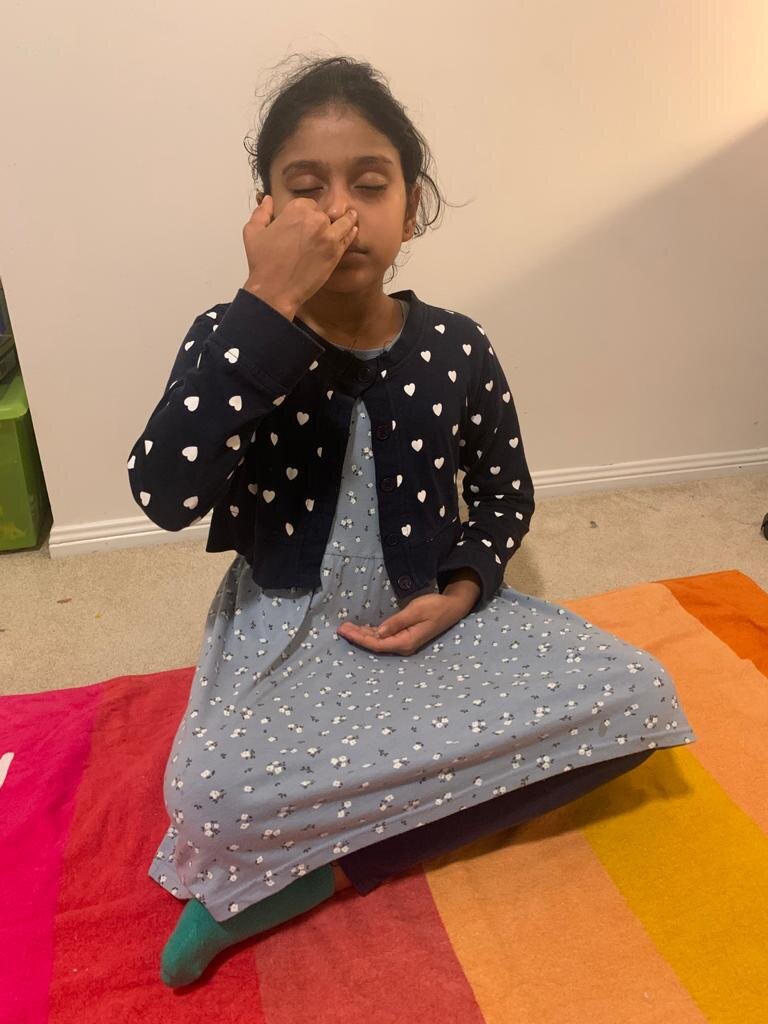 Child practicing yoga breathing exercise while sitting on floor with crossed legs.