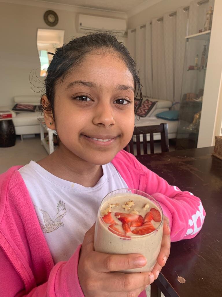 Girl holding a smoothie topped with sliced strawberries and nuts in a glass.