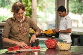 Two people in a kitchen preparing fruit, with one slicing watermelon and another working in the background.