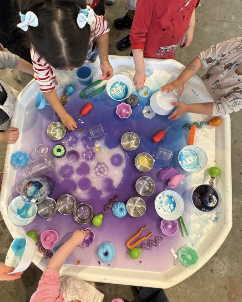 Children playing with a sensory table filled with colored water, foam shapes, and toys.