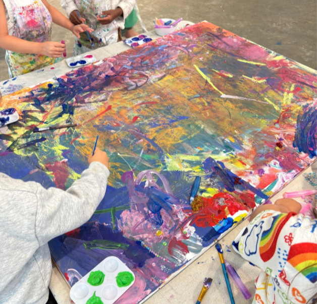 Children creating an abstract painting on a large canvas with colorful paints and brushes.