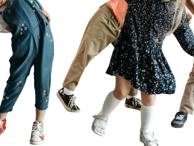 Close-up of three children’s legs and feet, wearing casual clothes and sneakers, jumping or dancing against a white background.