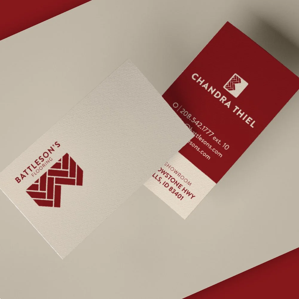 Business card for Battleson's Flooring in Idaho Falls, featuring a logo and contact information, placed on a beige surface with a white and red color scheme.