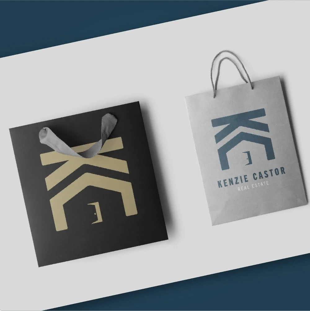 Two shopping bags with the logo and name of Kenzie Castor Real Estate, one black with beige logo, one white with blue logo, placed on a white and blue background.