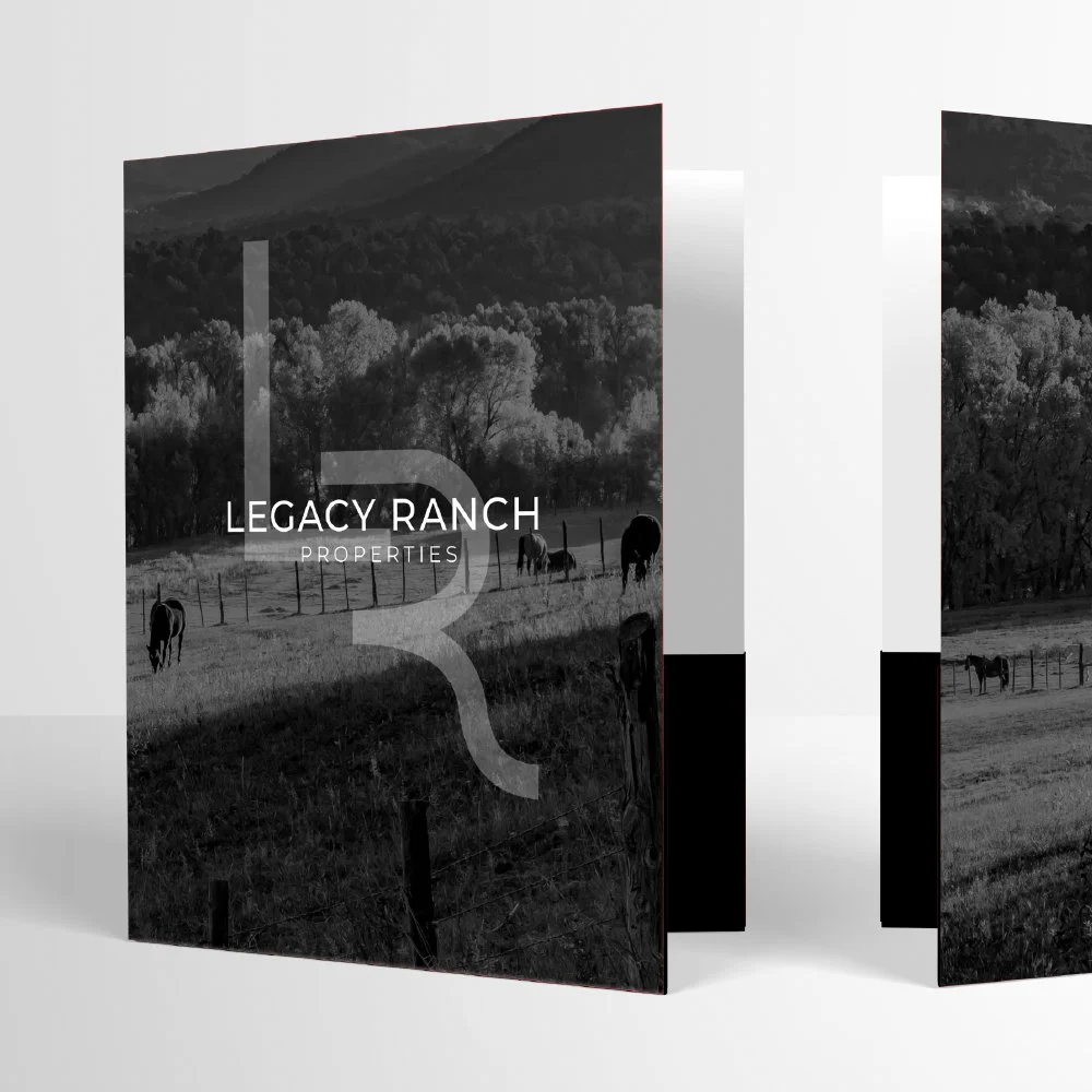 Brochure or catalog cover for Legacy Ranch Properties featuring a black and white photo of a ranch with horses grazing, trees, fencing, and hills in the background.
