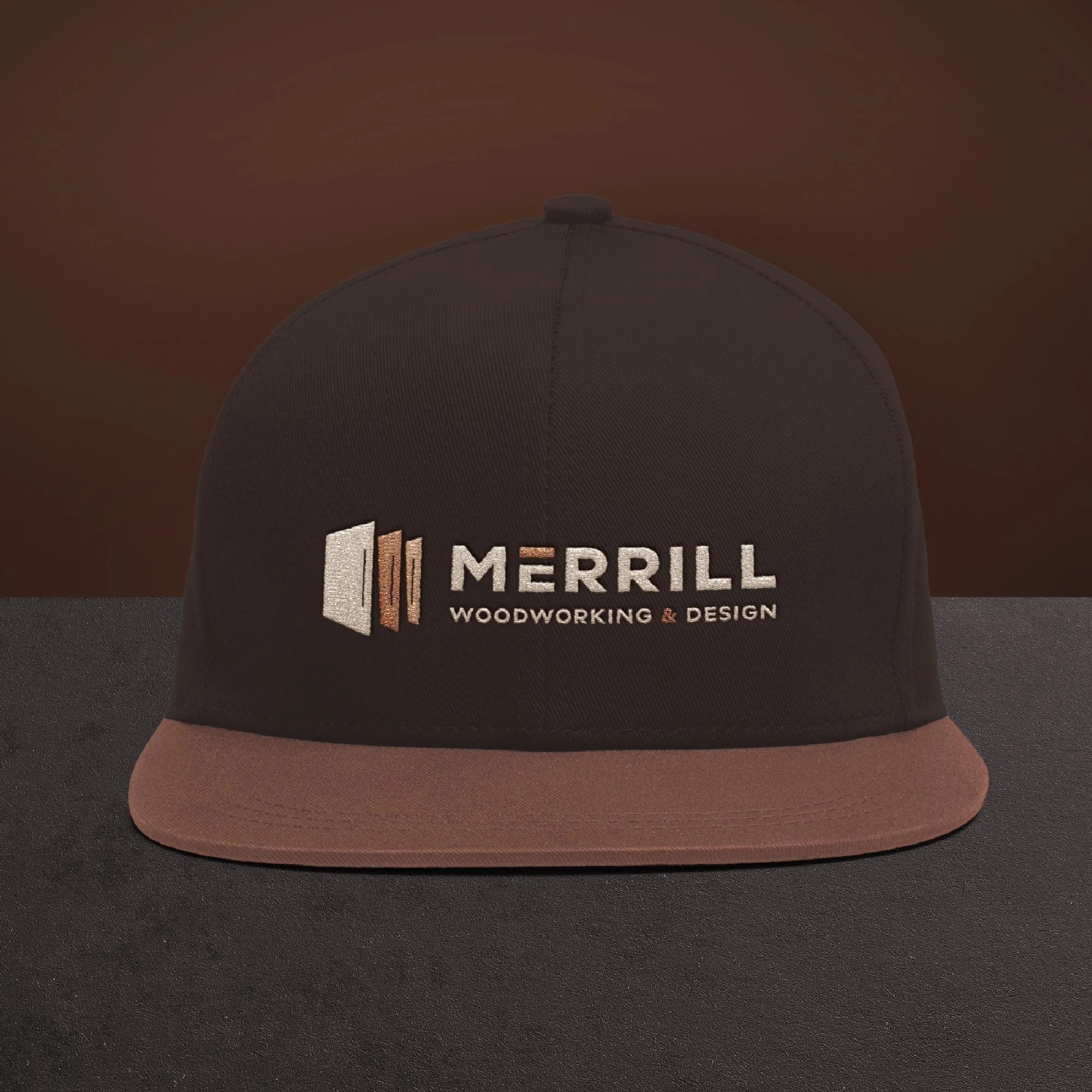 Black and brown baseball cap with embroidered logo and text 'MERRILL WOODWORKING & DESIGN' on front
