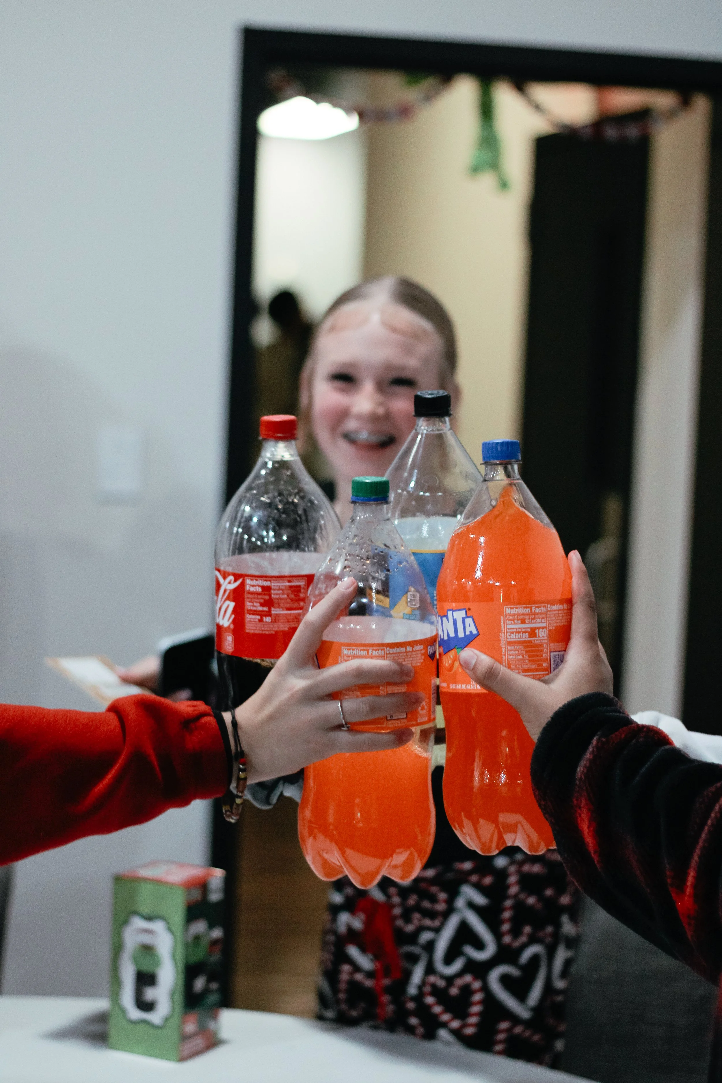 Children holding bottles of orange soda in celebration at a party, with a girl smiling in the background.