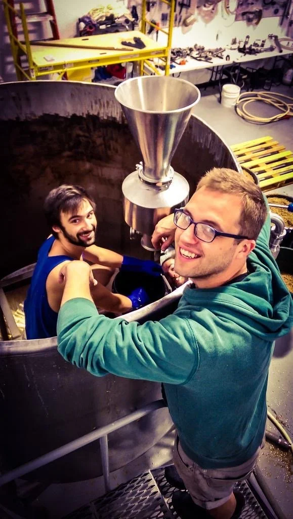 Alex Swanson inside the mash tun while cleaning it, with Joe Lemnah standing on the right at the early Williston brewery.
