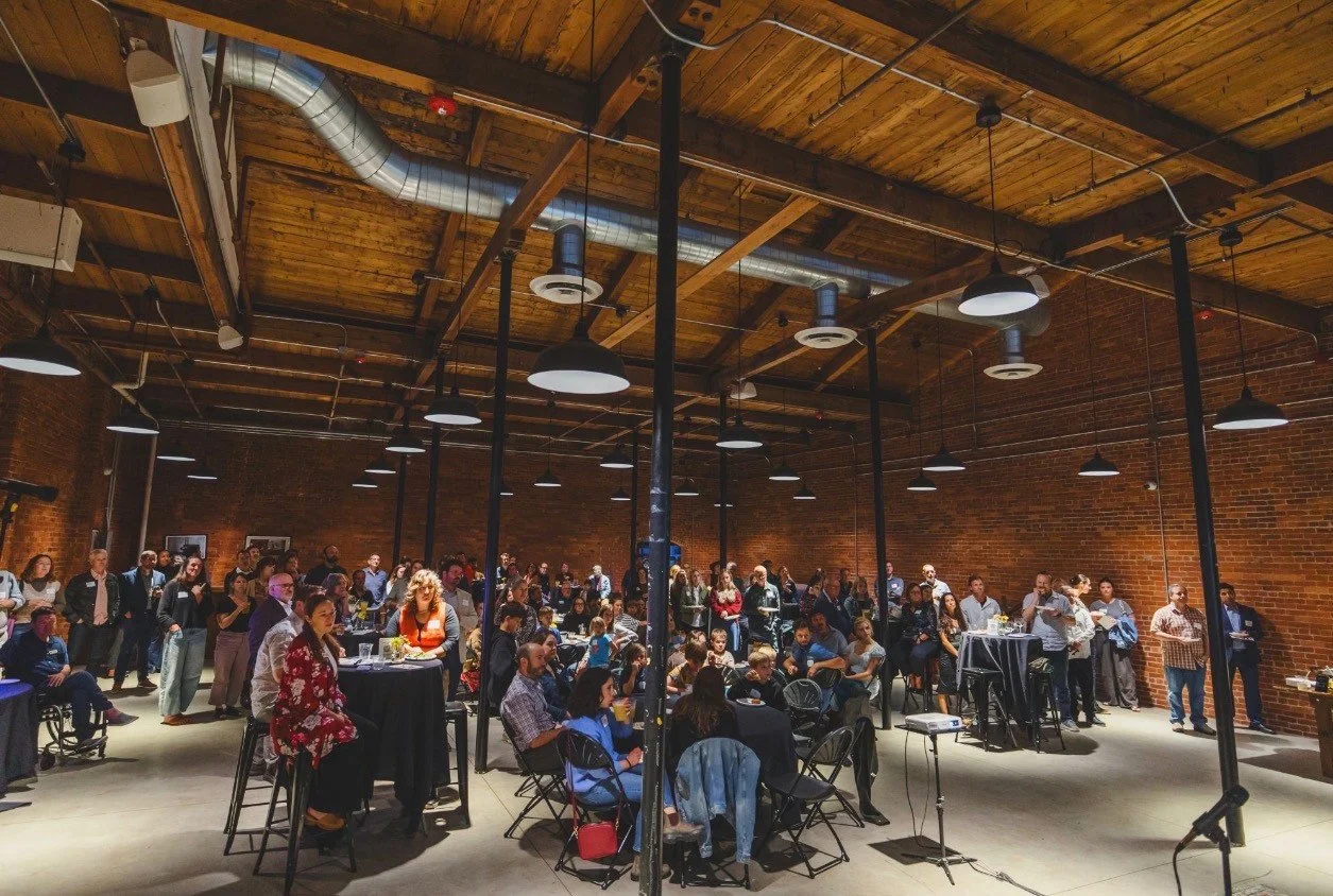 Guests gathered for an event in Lumière Hall at Burlington Beer Co., beneath timber beams and skylights.