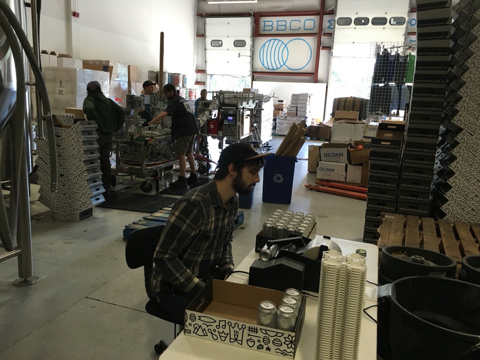 Burlington Beer Co. team members canning and packing beer beside stacks of can trays at the early brewery.