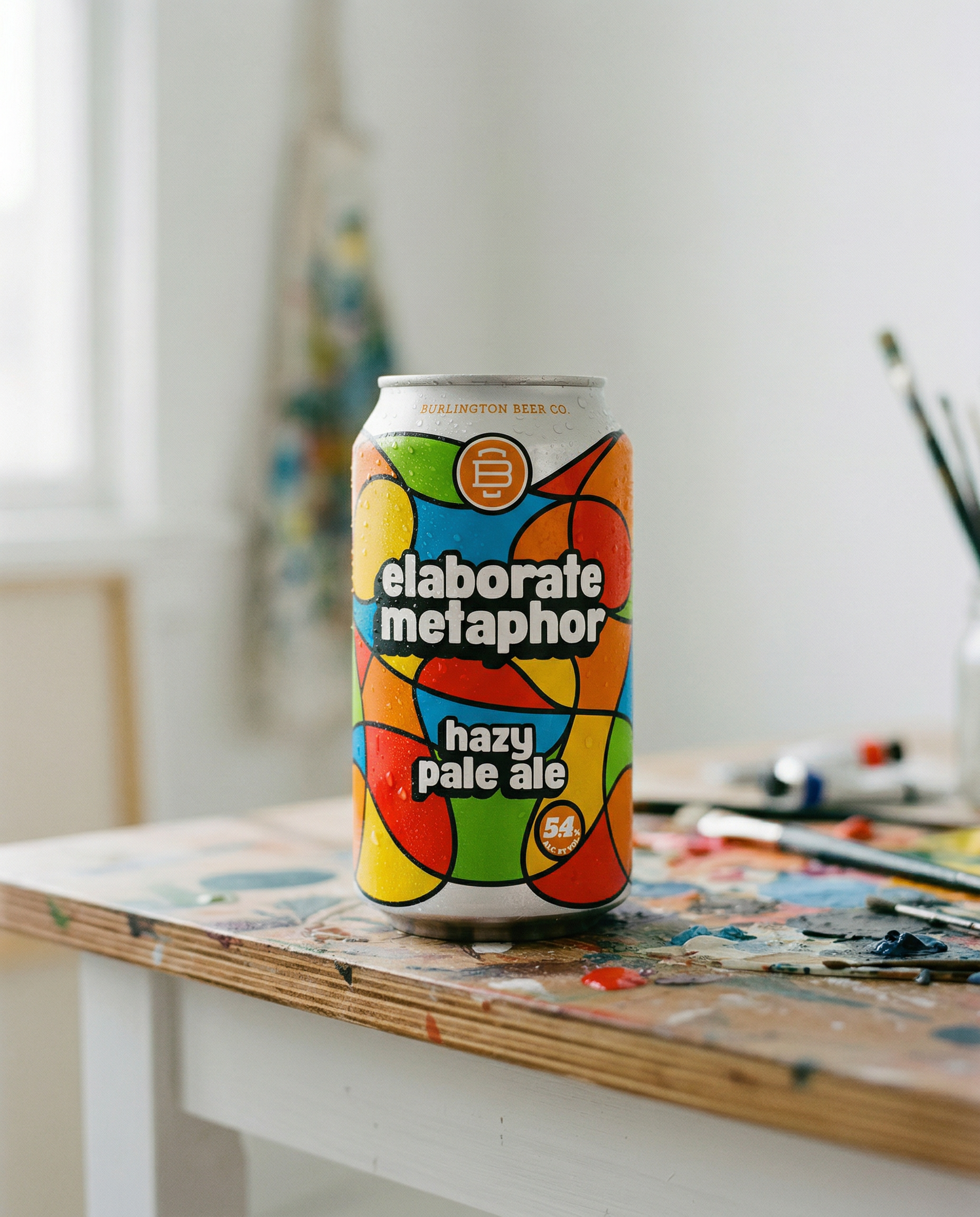 Elaborate Metaphor Hazy Pale Ale can surrounded by colorful art supplies